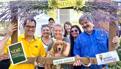 Faculty, staff and student holding a puppy posing in decorative photo frame.