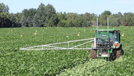 Green tractor with pesticide spray rig in green field. 