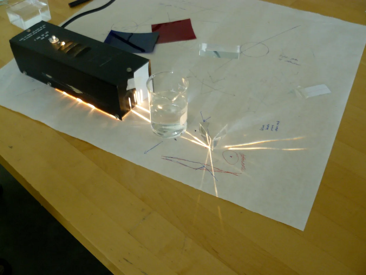 Physics equipment emitting light next to a glass of water.