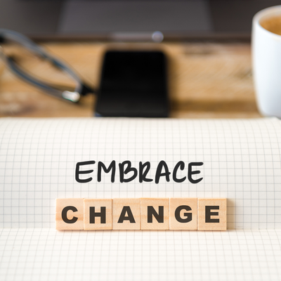 Image of desktop with phone, glasses in background. Foreground is the words Embrace Change. 