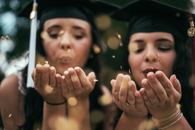 Two girls in graduation caps blowing kisses