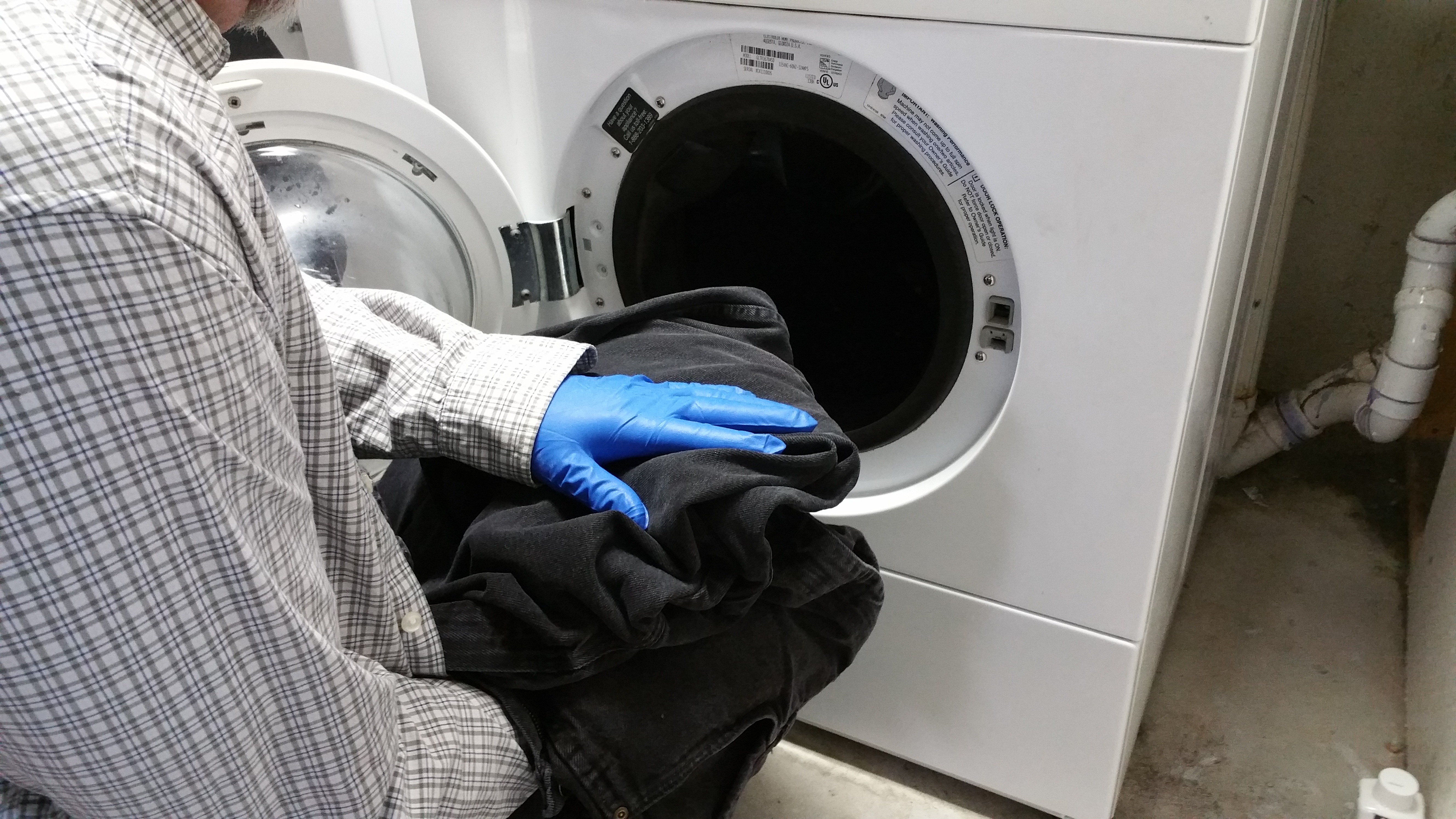 Man with latex gloves and long sleeves putting clothes in a washer
