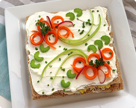 Swedish sandwich cake covered with cream cheese & yogurt frosting and decorated with red and green vegetables.