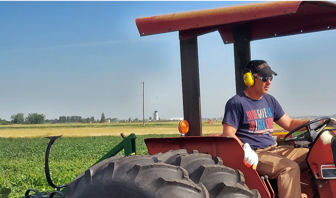 man wearing earmuff hearing protection driving a tractor on a sunny day
