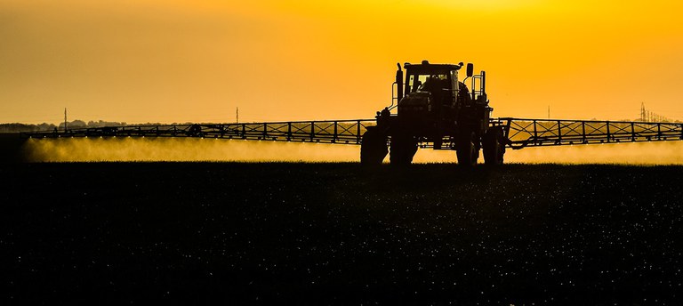 Silhouette of tractor spraying at sunset