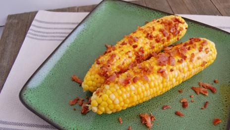 photograph of 2 piece of corn on the cob with bacon on a green plate