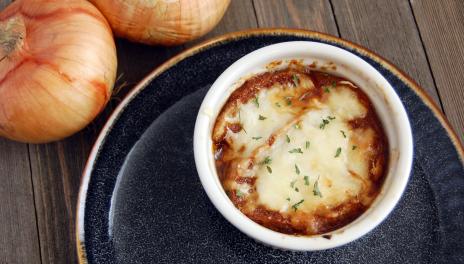 photograph of a bowl of french onion soup on a plate with two onions next to it