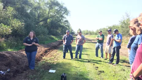 woman standing next to manure compost pile talking to a crowdabout