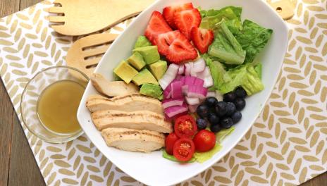 grilled chicken salad in bowl with side of dressing