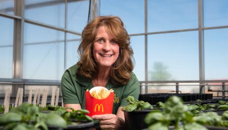 Woman in greenhouse holding a McDonald’s container of French fries. 