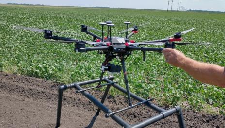 A drone sits on the fine soil at the edge of a bean field.