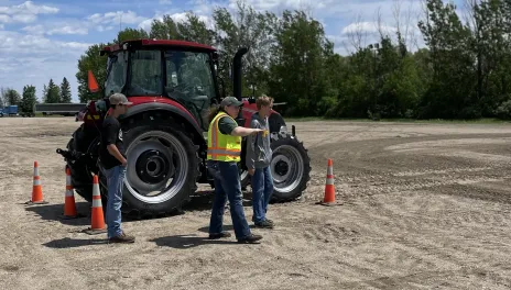 Person in yellow safety vest stands in front of red tractor talking about tractor safety. 