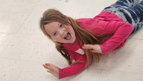 Young girl in pink shirt lays on floor. 