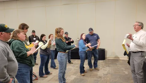 Several standing people take notes as an instructor demonstrates a crop pest.