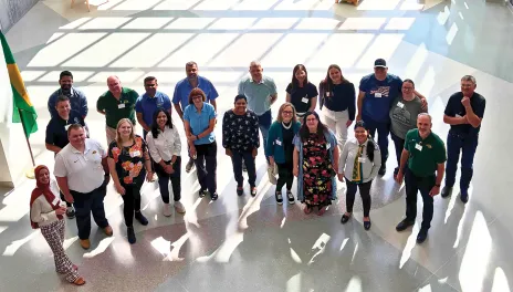 A group of people standing together in a bright indoor space with sunlight casting grid-like shadows.