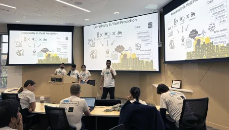 Participants present a yield‑prediction project in a classroom with slides displayed on two large screens