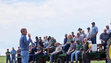 a man speaking to a group sitting on a trailer in a field