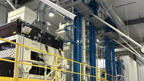 Large cleaning equipment, with ductwork and catwalks, inside a metal building with a cement floor.