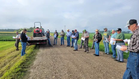A group of farmers stand on a gravel road near test plots.