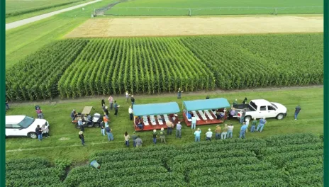 An aerial view of two covered wagons in a reseach plot, surrounded by people.