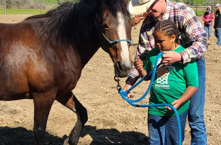 Photo of youth learning how to hold a horse halter at North Dakota 4-H Camp. Youth is learning from cowboy instructor.