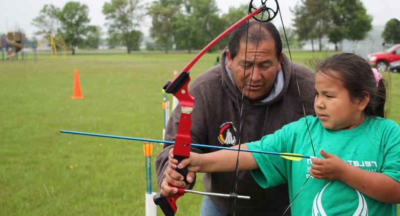 A 4-H volunteer helps a 4-H kid practice archery