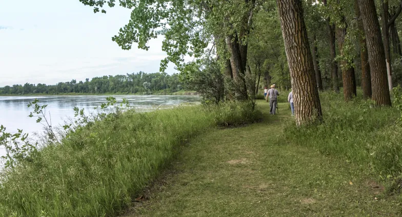 two people walking on a path next to a river