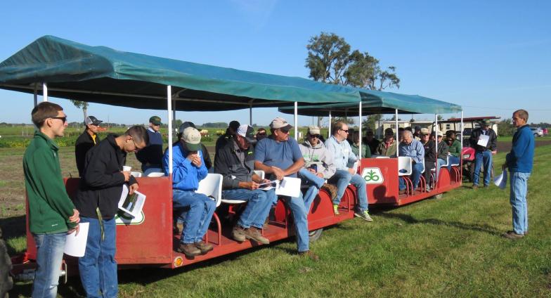 About 30 people are pictured riding on two red trailiers with seats and green canopies at the 2017 Oakes Irrigation Site Field Day.
