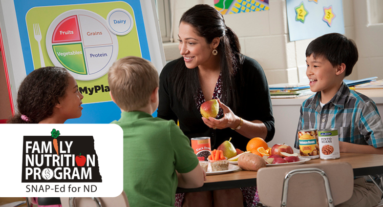 The Family Nutrition Program, SNAP-Ed for ND logo superimposed over a photo of a teacher and young students eating lunch.