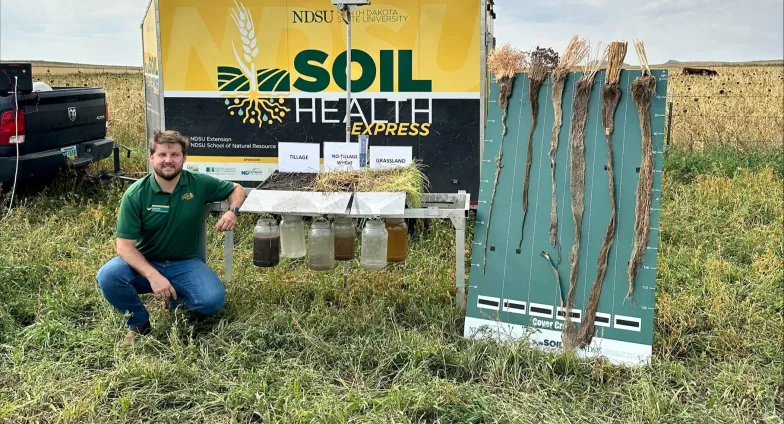 carlos poses with a soil health exhibit in front of Soil Health Express trailer