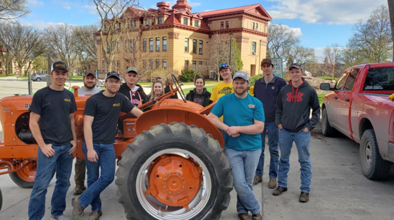students posing with a red tractor