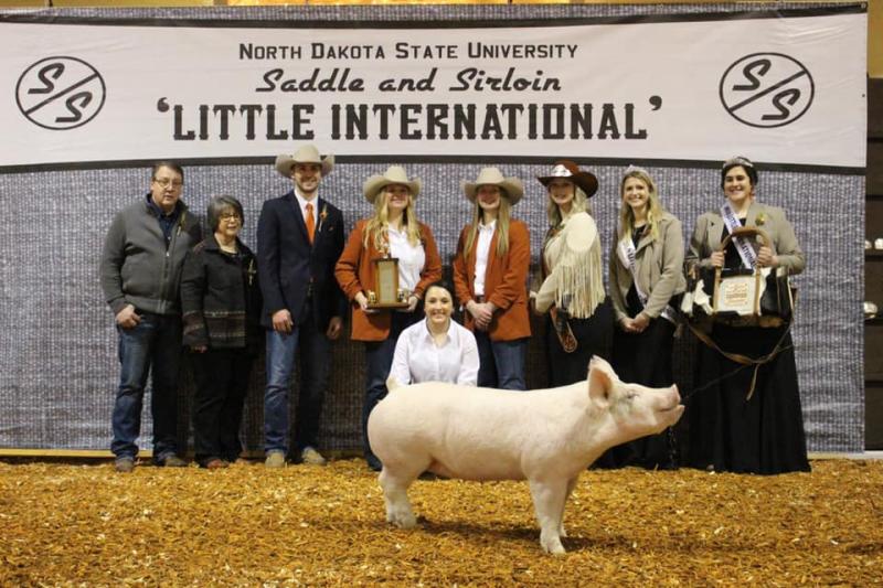 members pose behind a pig in an arena with a banner in the background