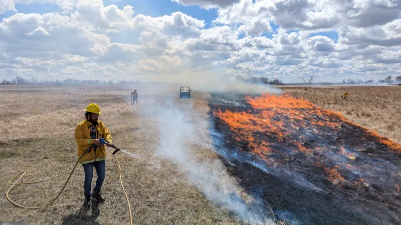 A man puts water on a controlled prairie burn
