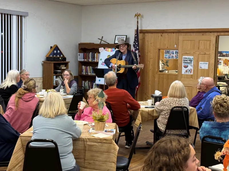 people at tables listening to a man playing a guitar