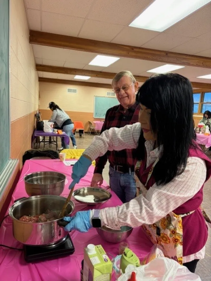 A woman stirring food in a crock pot while a senior citizen observes
