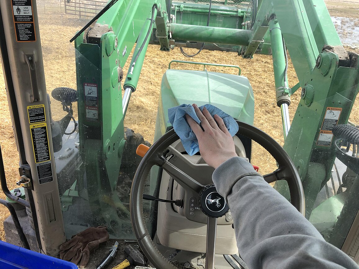 A photo from inside a tractor cab showing the driver wiping down the steering wheel
