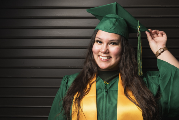 Photo of NDSU graduate, Class of 2023, Ambrosia Yellow Bird, smiling wearing an NDSU graduation gown and mortarboard with green/yellow tassel.