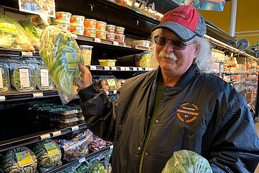 A man holding a head of lettuce in a grocery store