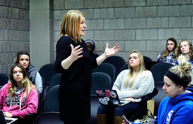 Photo of Dena Wyum standing and speaking to a classroom of students in an auditorium