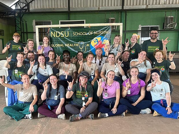 Group of NDSU Nursing students posing in front of a poster showing the Go Bison horns-up sign with their hands.