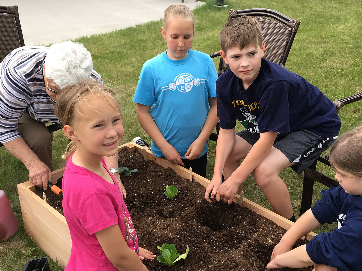 Three 4-H'ers and a 4-H volunteer are gathered around a container garden with their hands in the soil.