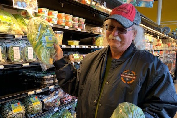 A man holding a head of lettuce in a grocery store. 