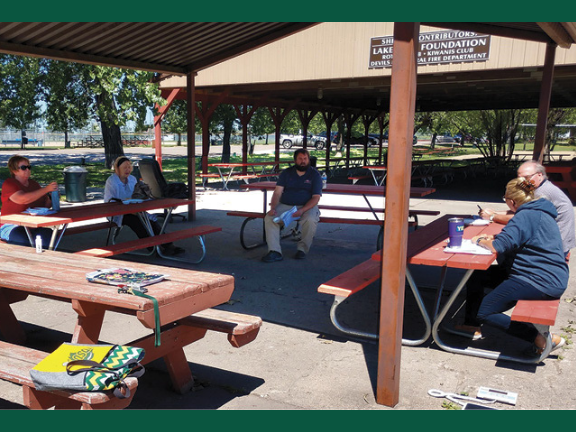 Particioants in the Diabetes Prevention Program sit, socially distanced, at red picnic tables under a park shelter.