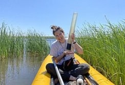 Christine Cornish (fellow) sitting in a boat holding a freshly collected sediment core