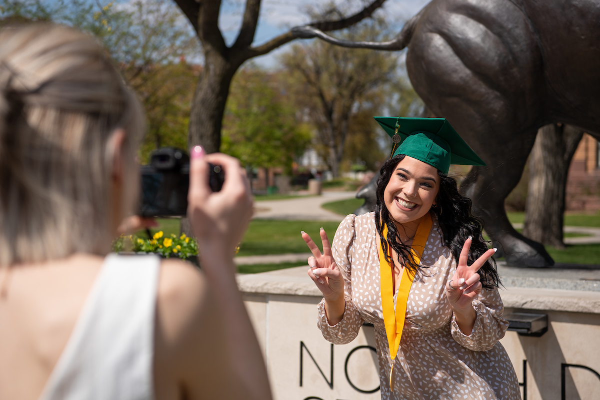 Student at the Bison statue during commencement