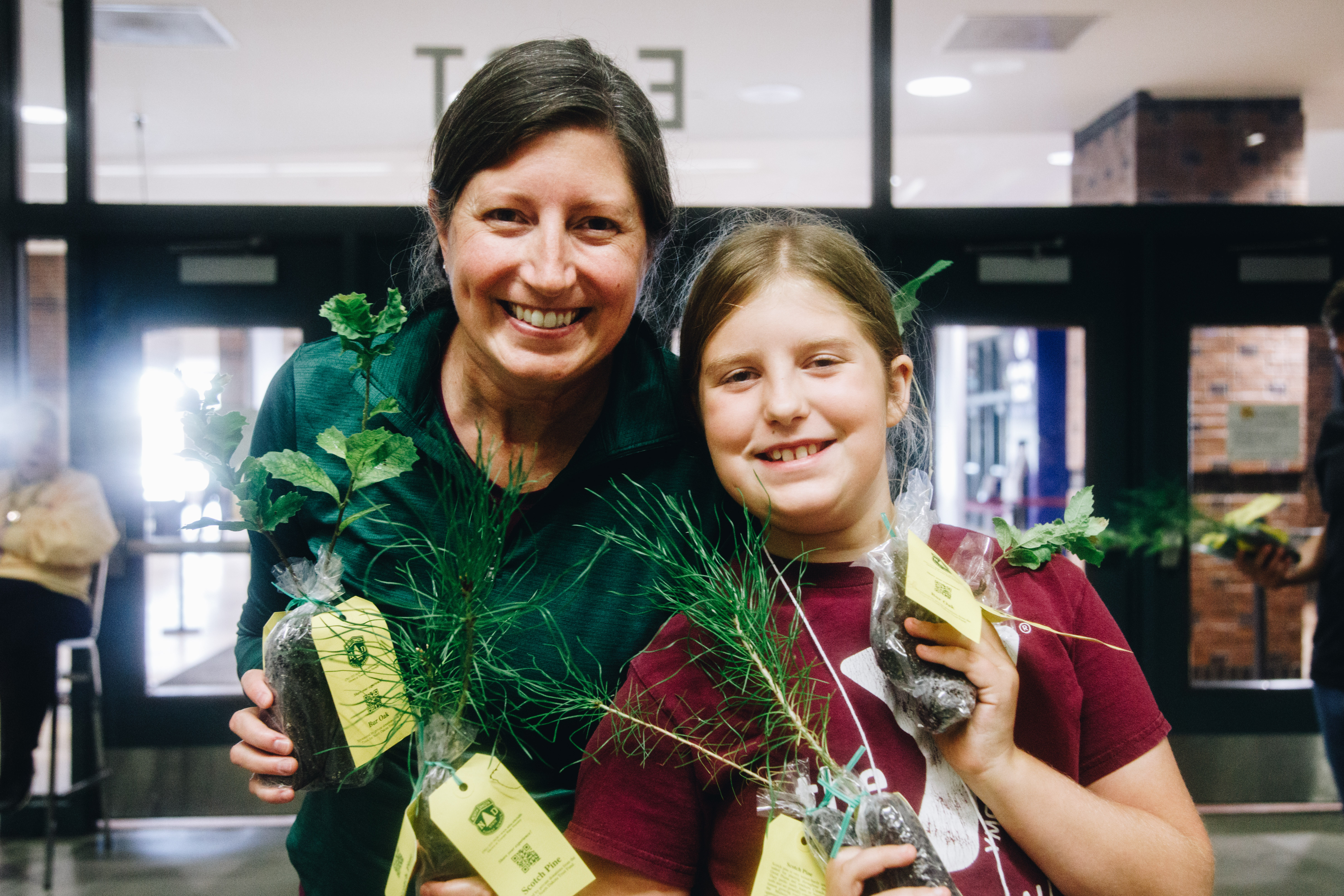 A woman and her daughter smiling while holding tree seedlings