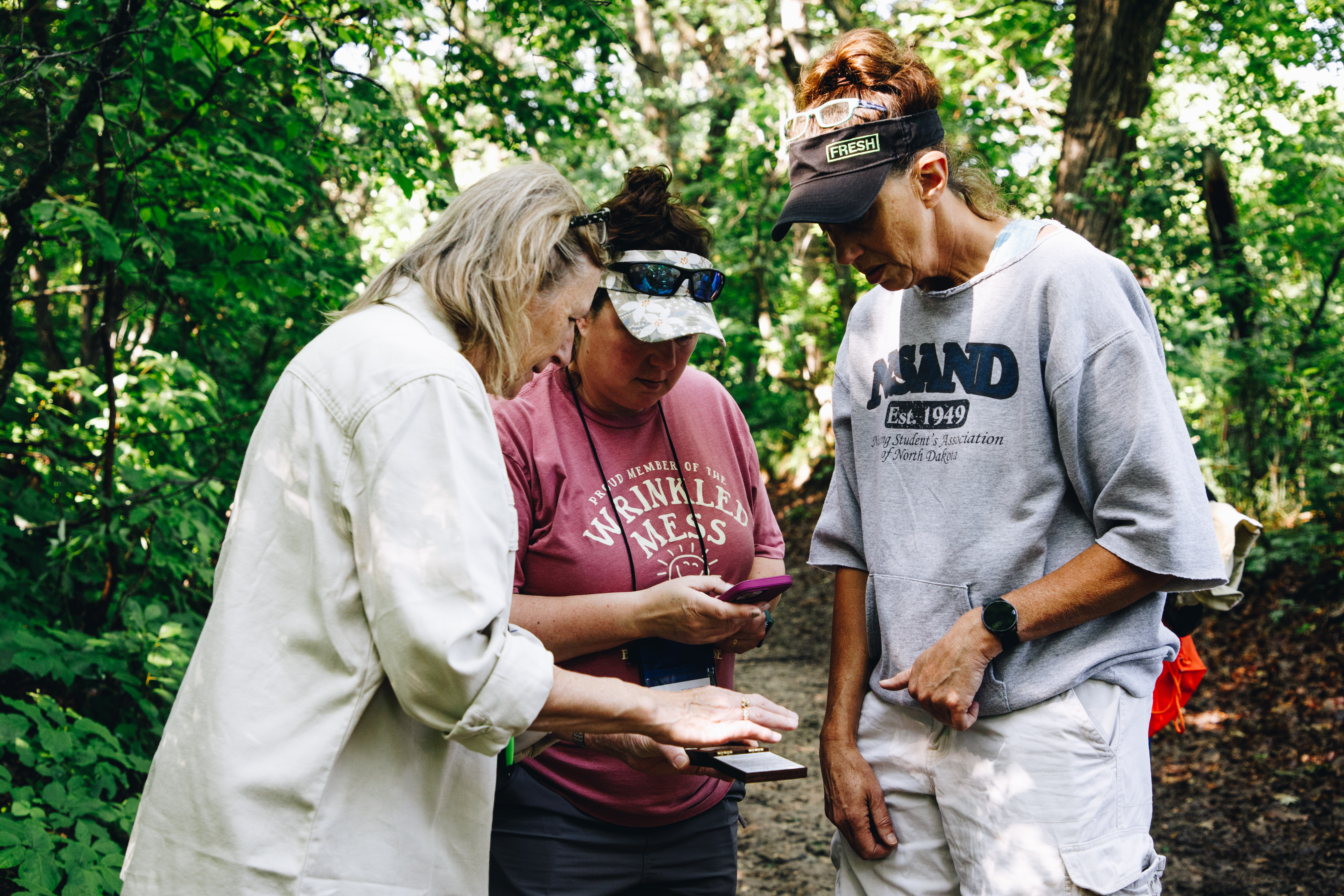 Three educators look at a forestry tool that measures forest canopy cover in a forest
