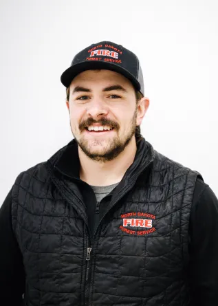 A man with a brown mustache and beard smiling and wearing a baseball cap