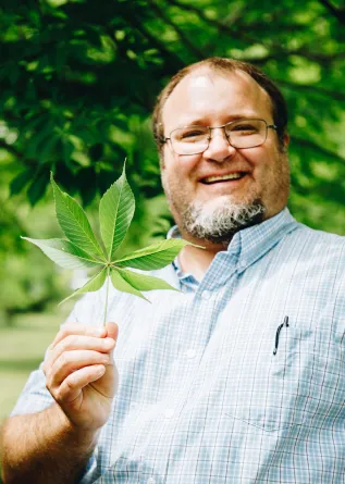 man smiling holding up a leaf from a tree