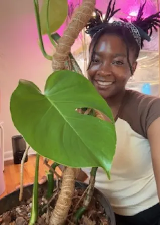 Student smiling and holding a Monstera leaf.